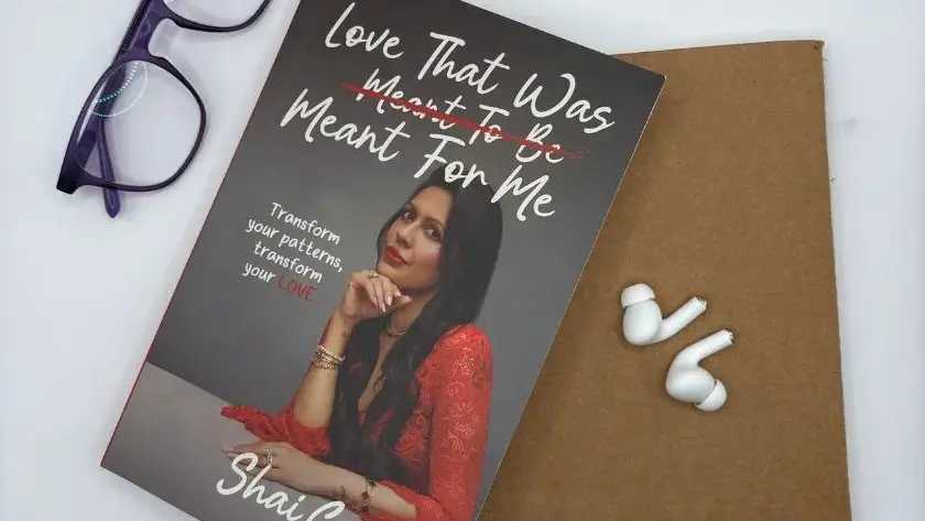 Book cover and white earbuds on gold surface with woman in red shirt