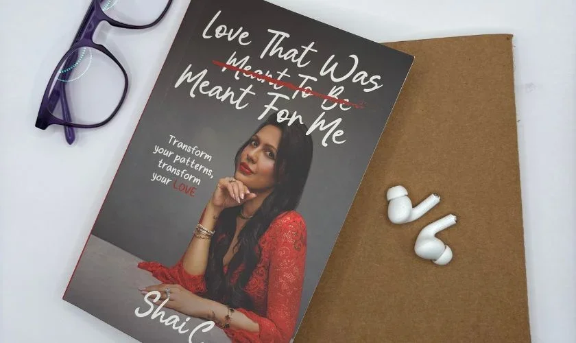 Book cover and white earbuds on gold surface with woman in red shirt